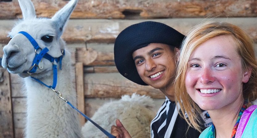 Two people smile at the camera while posing with a llama.